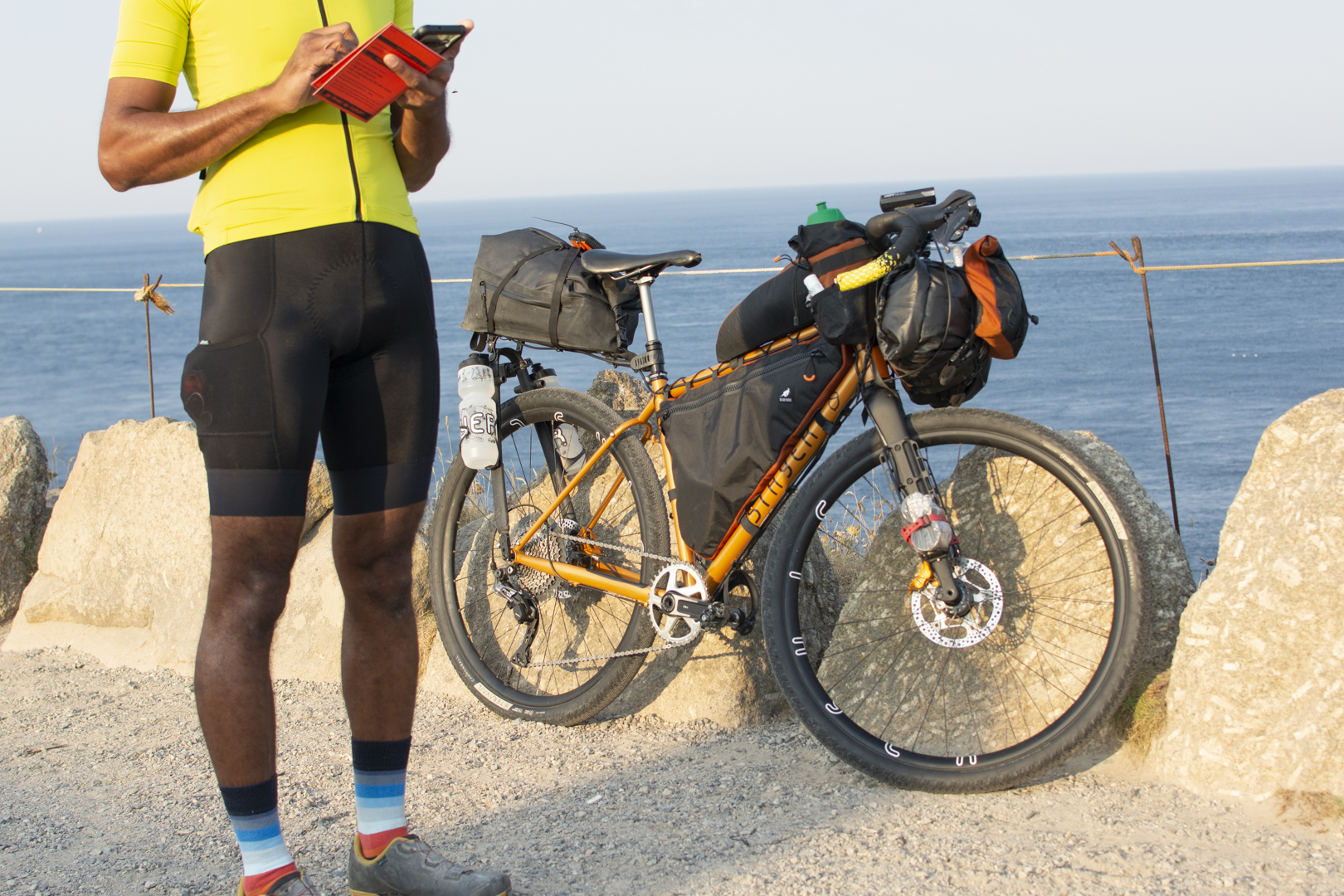 Aandy on the startline of GBDURO standing beside his bike, brevet card in hand, next to the sea.